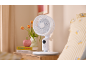 Ventilateur de table blanc sur une table de chevet en bois à côté du lit.