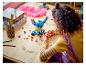 Enfant construisant une figurine LEGO Stitch bleue sur une table en bois.