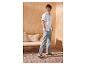 Homme en chemise blanche à manches courtes, pantalon gris et sandales noires dans un décor méditerranéen.