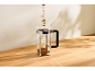 Café versé dans une cafetière à piston en verre sur une table en bois.
