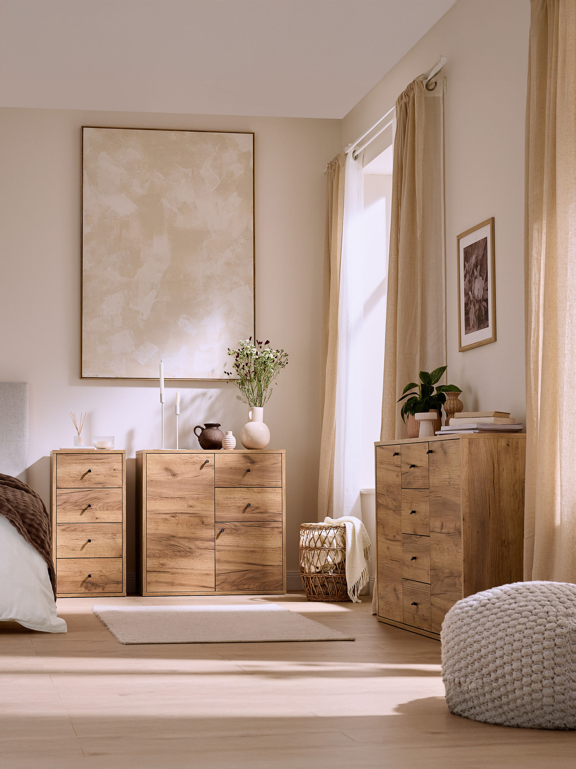 Chambre à coucher lumineuse avec commodes en bois clair, lit et pouf tricoté.