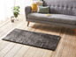 Un tapis gris devant un canapé gris dans un salon clair.