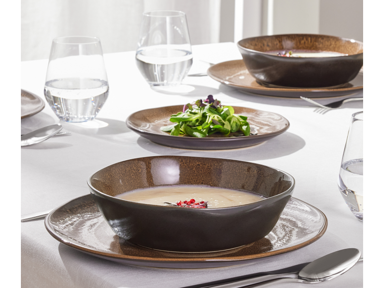Table dressée avec des bols et assiettes en céramique marron foncé, des verres d'eau et des couverts.