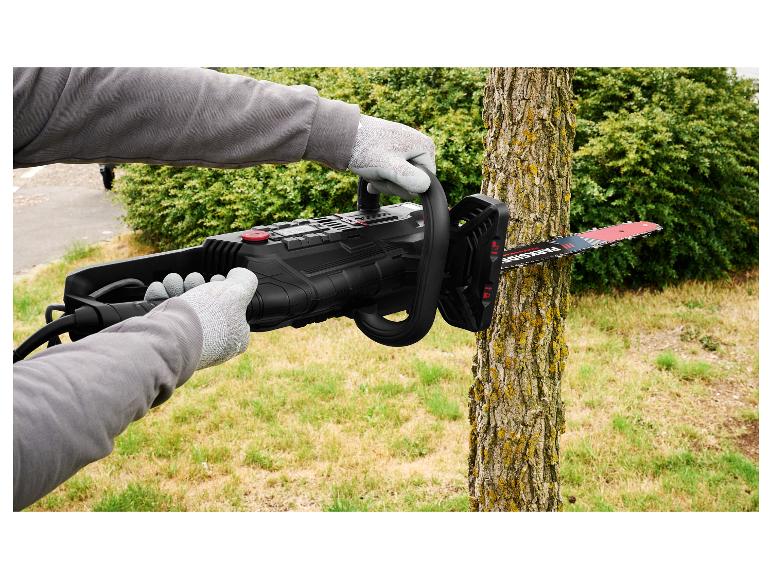 Personne gantée utilisant une tronçonneuse électrique noire pour couper un tronc d'arbre dans un jardin.