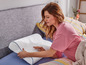 Une femme teste un oreiller blanc avec une bordure bleue sur un lit.