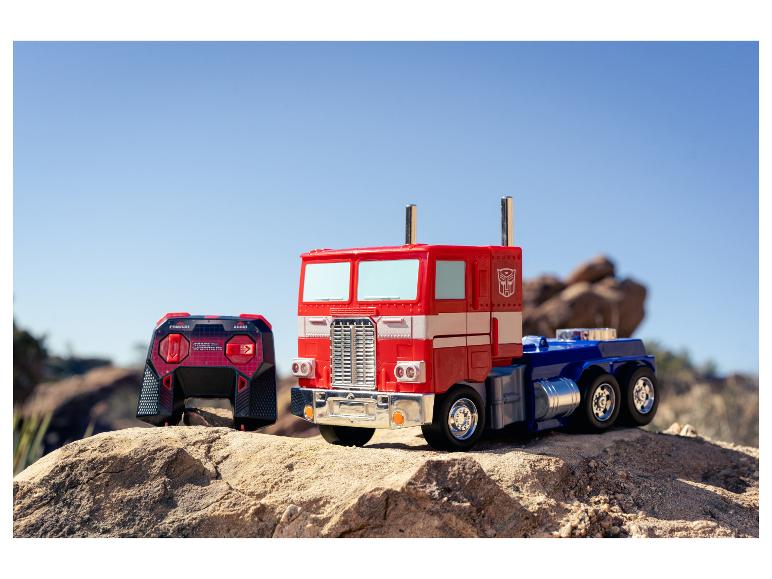 Un camion jouet Optimus Prime et une télécommande sur un terrain rocheux sous un ciel clair.