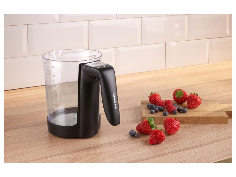 Pichet doseur avec poignée et baies sur un comptoir en bois.