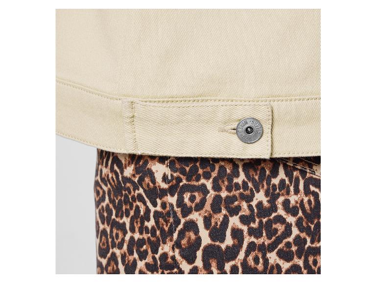 Gros plan d'une veste en jean beige avec un bouton, portée sur un pantalon imprimé léopard.
