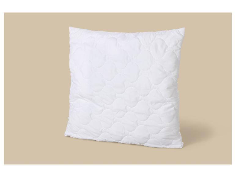 Oreiller blanc matelassé avec un motif ondulé sur fond beige.