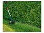 Une tondeuse à gazon verte tond l'herbe le long d'une haie.