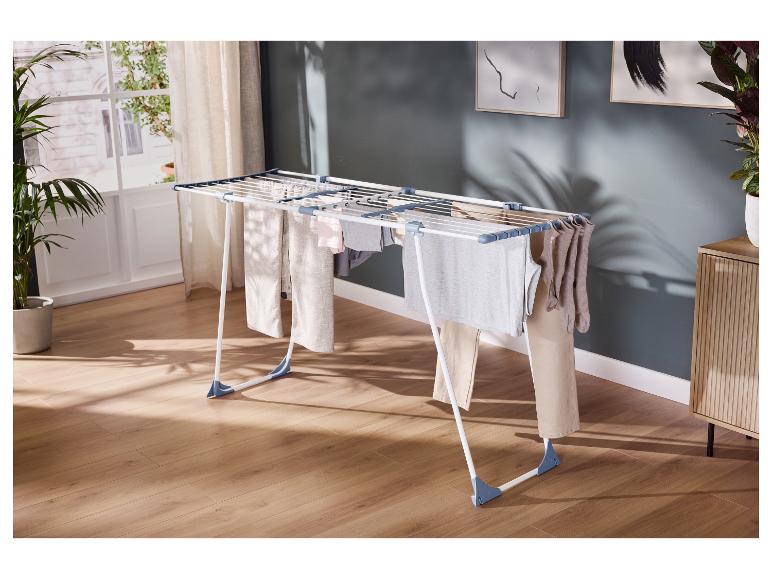 Séchoir à linge avec divers vêtements dans une pièce lumineuse au sol en bois.