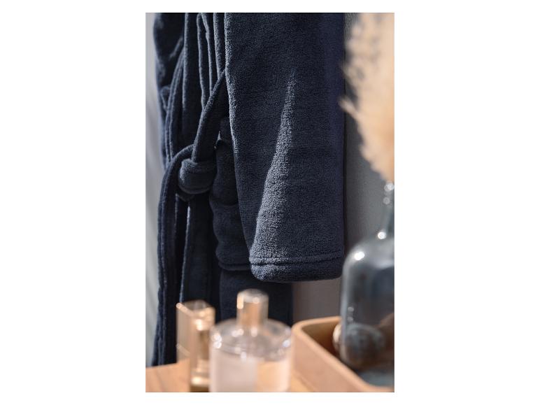 Peignoir bleu foncé suspendu à côté d'un vase de fleurs séchées et de flacons de parfum.