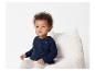 Bébé en pull bleu marine assis dans un fauteuil moelleux.