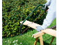 Homme coupant une planche de bois avec une scie sur un tréteau en bois dans le jardin.