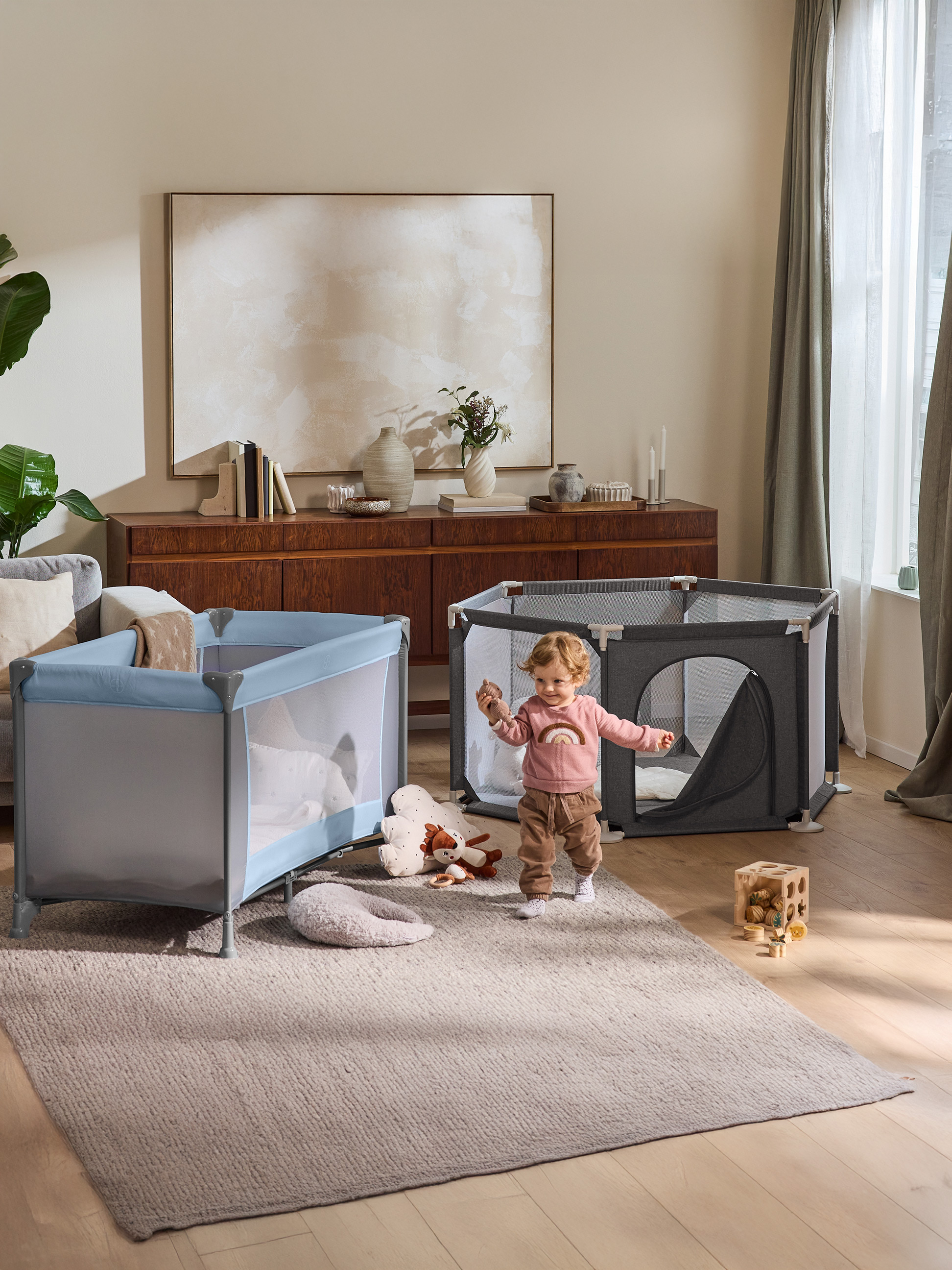 Un bambin joue dans le salon avec un parc et un lit de voyage.