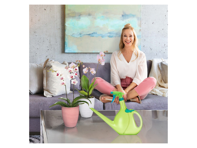Une femme arrose des orchidées avec un arrosoir vert.