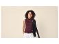 Femme en top col roulé sans manches couleur vin et pantalon blanc, tenant un cardigan noir.