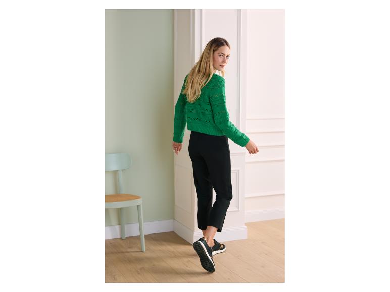 Femme en pull tricoté vert et pantalon noir, s'éloignant et regardant en arrière.