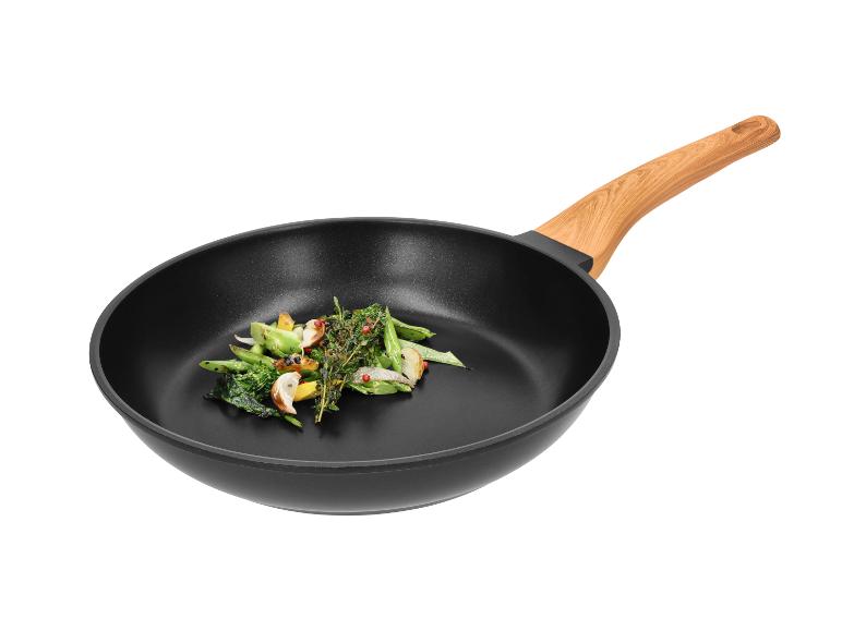Poêle noire avec manche en bois et légumes sautés.