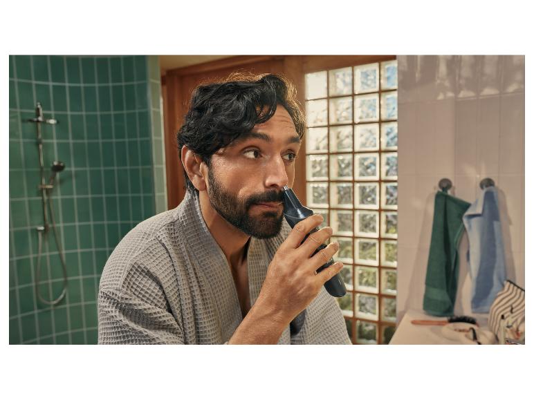 Un homme en peignoir gris utilise un rasoir électrique pour le nez et les oreilles.