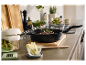 Une poêle noire avec un steak et des herbes, entourée d'ingrédients et d'ustensiles de cuisine.