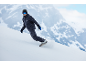 Snowboarder en combinaison de snowboard bleu foncé dévalant une piste de montagne enneigée.