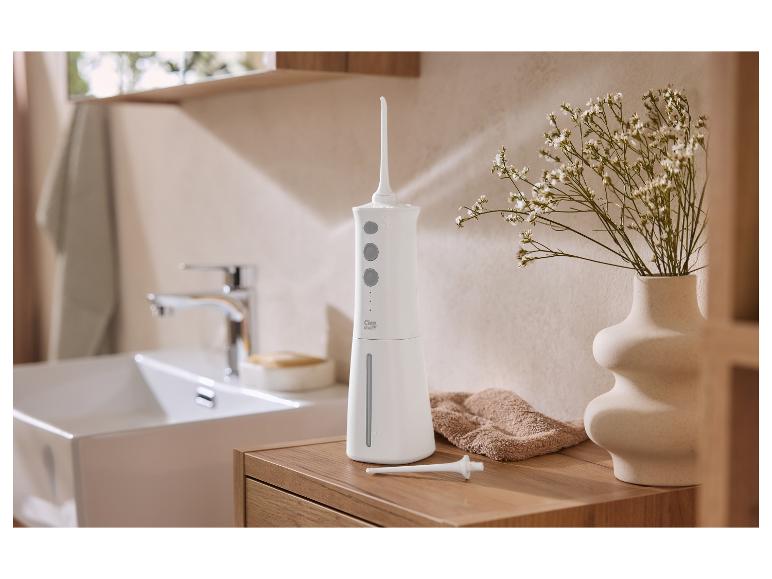 Hydropulseur blanc sur un meuble de salle de bain en bois, à côté d'un vase de fleurs.