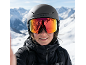 Femme avec masque de ski et casque devant des montagnes enneigées.