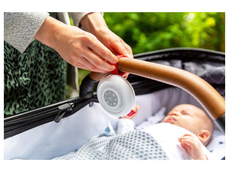 Un parent attache une machine à sons blanche ZAZU à la poignée d'une poussette au-dessus d'un bébé endormi.