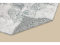 Tapis à motifs gris et blanc avec un coin relevé, révélant le dos antidérapant.