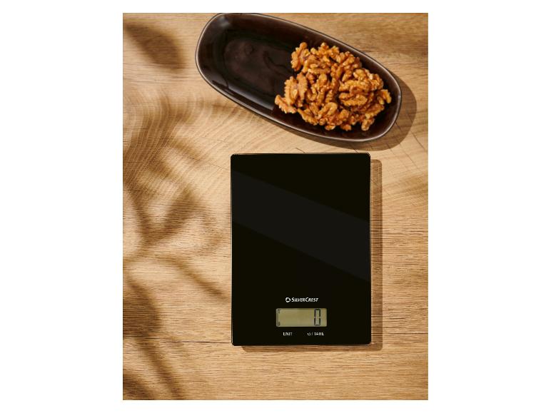 Une balance de cuisine noire SilverCrest sur une table en bois avec des noix.
