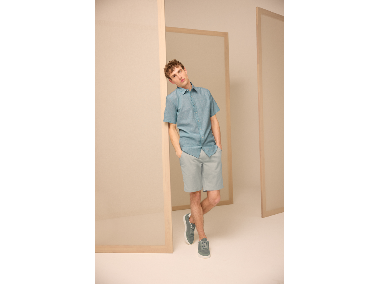 Homme en chemise bleu clair à manches courtes, short gris et baskets.