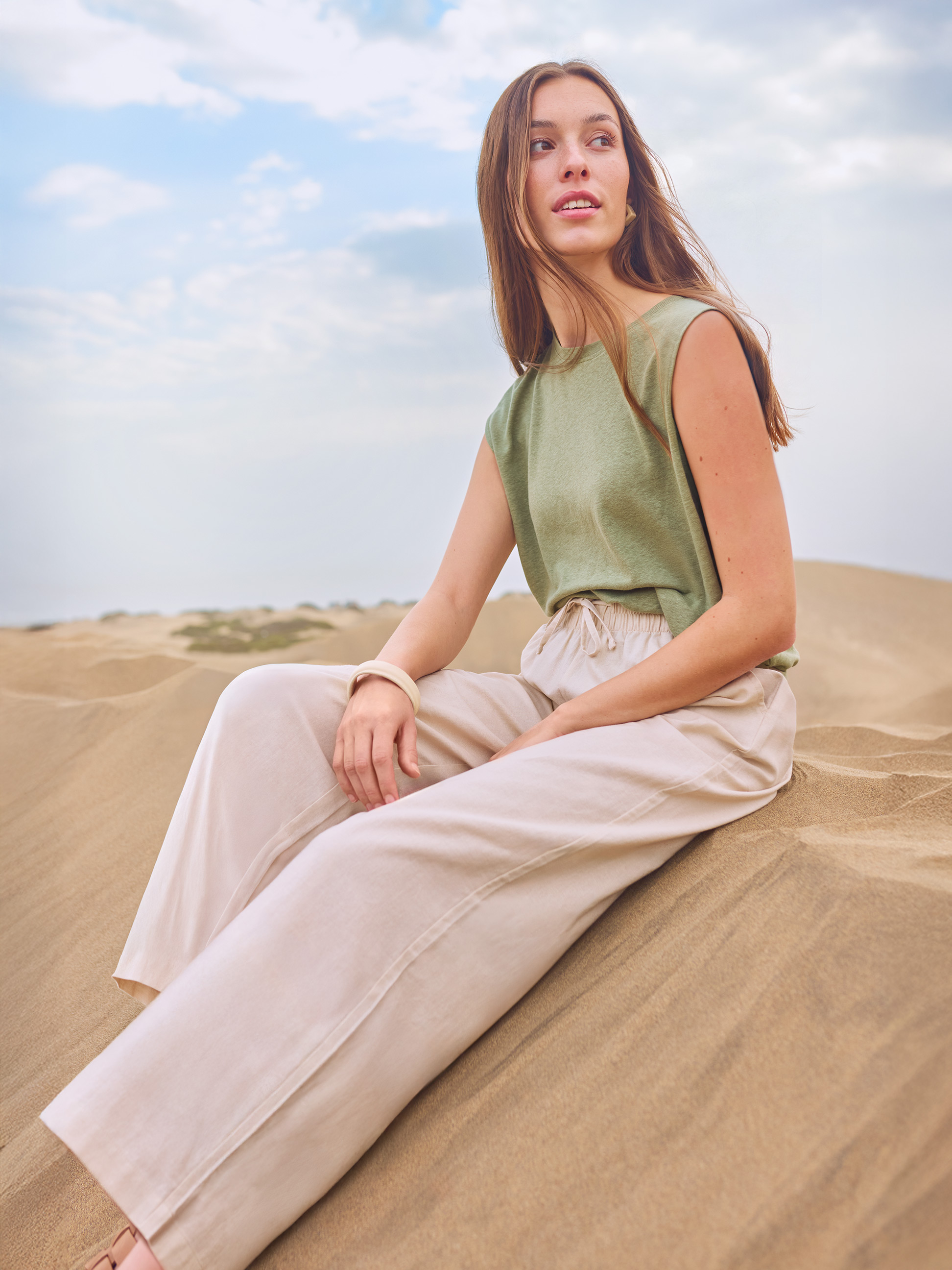 Femme en t-shirt vert et pantalon beige assise dans les dunes de sable.