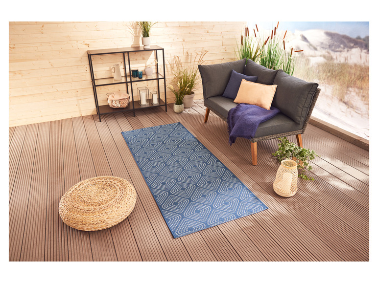 Un tapis extérieur bleu avec un motif géométrique sur une terrasse en bois.