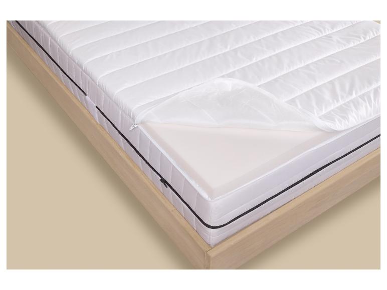 Matelas blanc avec fermeture éclair ouverte montrant la mousse intérieure, sur un cadre de lit en bois.