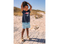 Une fille porte un t-shirt bleu avec un imprimé sirène et un short en jean bleu sur la plage.