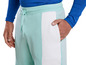 Un homme porte un haut bleu à manches longues et un pantalon de survêtement vert menthe avec des détails blancs.