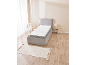 Lit simple avec revêtement gris, matelas blanc et tapis sur un parquet en bois.