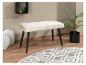 Un banc de couleur crème avec des pieds noirs sur un tapis à motif géométrique gris et blanc.