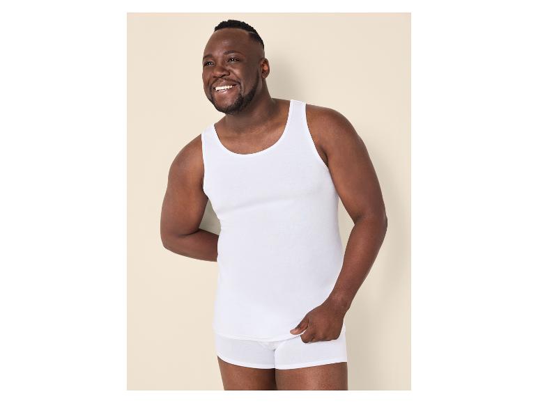 Homme en débardeur et caleçon blancs, souriant.