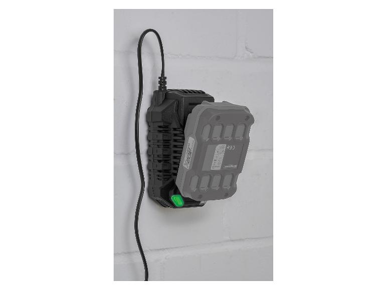 Chargeur noir avec une batterie grise attachée, monté sur un mur de briques blanches.