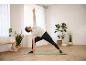 Homme faisant du yoga sur un tapis vert dans une pièce chaleureuse.