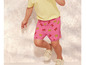 Un enfant porte un short rose à imprimé tigre et des baskets blanches.