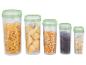 Cinq récipients transparents avec couvercles verts, remplis de pâtes, maïs, café et avoine.