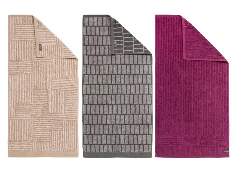Trois serviettes de bain : beige à motifs géométriques, grise à motifs de briques, et fuchsia unie.