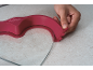 Main utilisant un ustensile de cuisine rose pour racler une surface transparente.