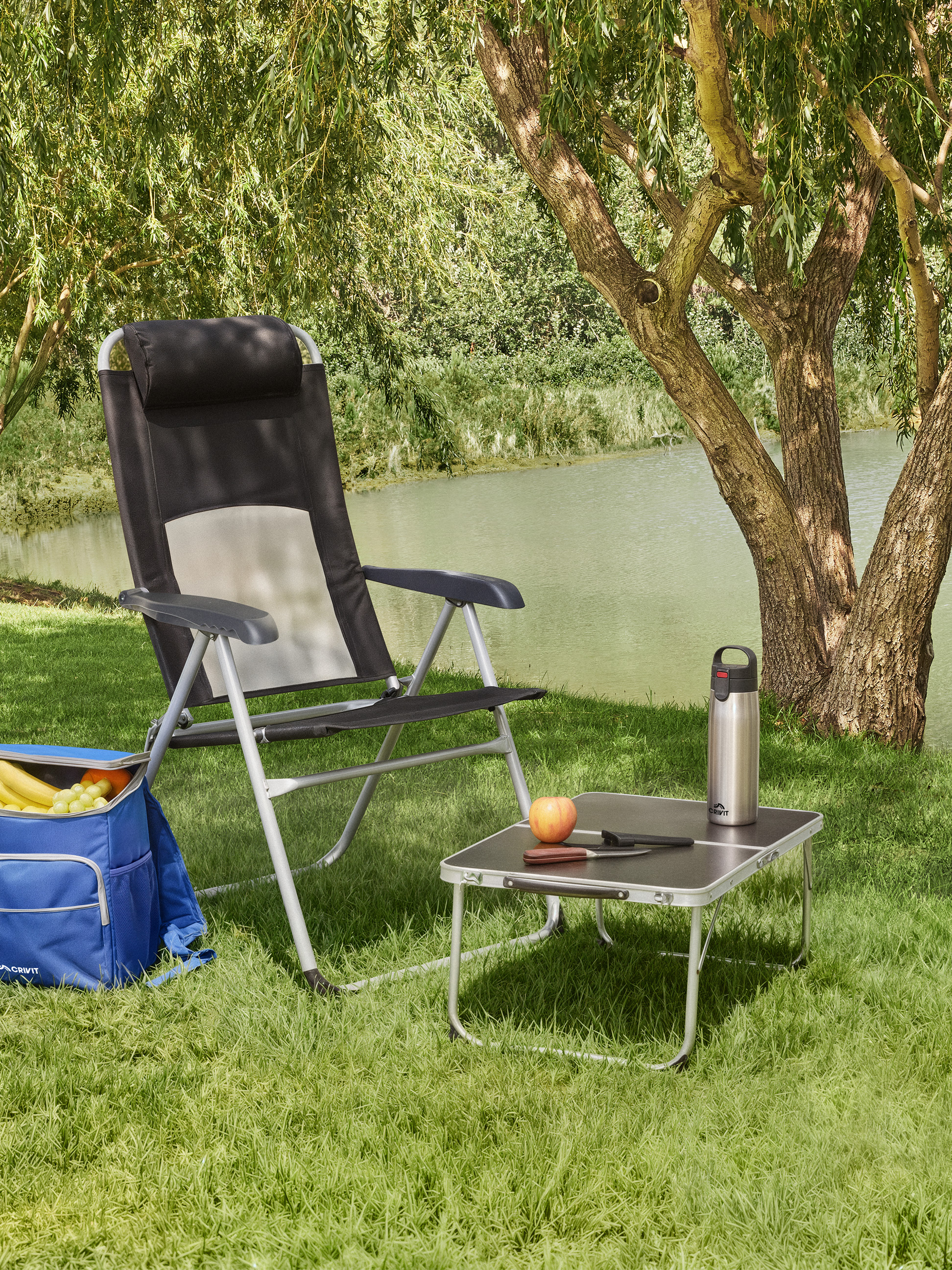 Chaise de camping pliable, petite table, sac isotherme et bouteille d'eau au bord d'un lac.
