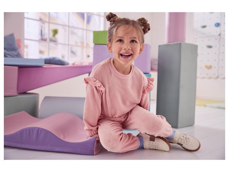 Fille joyeuse en ensemble rose assise sur le sol entourée de tapis de jeu doux.