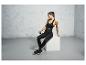 Femme en soutien-gorge de sport, leggings et baskets noirs, assise sur un cube.