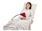 Une femme assise dans un fauteuil avec un coussin chauffant et une couverture douce.
